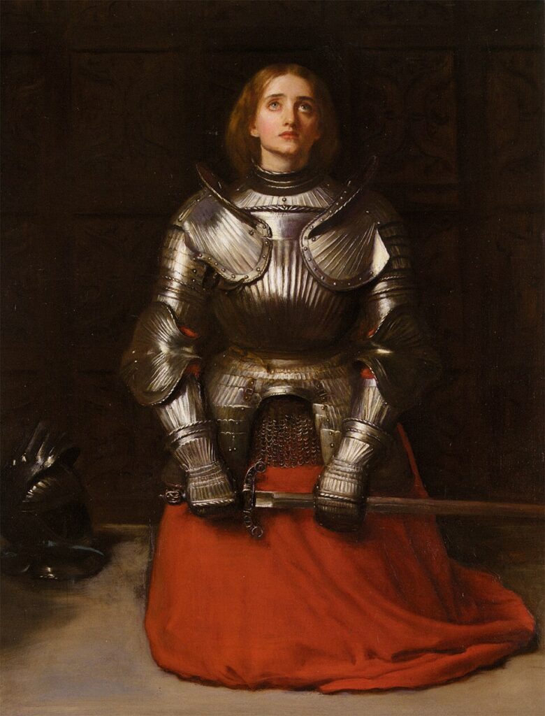 John Everett Millais, Joan of Arc. Diz çökmüş, zırhlı Jeanne kılıcını yatay tutar ve yukarı bakar; yerde miğfer, arkada koyu ahşap fon.
Pre-Raphaelite netlik, kırmızı kumaşın ateşi ve metalin soğuk parıltısıyla kurulmuş içsel yemin sahnesi.
Kaynak: https://commons.wikimedia.org/wiki/File:John_Everett_Millais_-_Joan_of_Arc.jpg