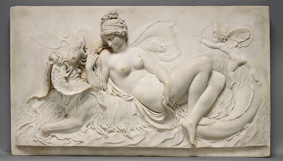 Mermer kabartmada Venüs, kıvrılan bir deniz canavarının (ketos) sırtında gevşekçe uzanır; sağda Cupid okunu gerer, arkada putto meşalesini kaldırır.
Draperi ile dalga aynı kıvrım diline bağlanır; ipek ten–pullu yele karşıtlığı erotizmi “neoklasik zarafet”e tercüme eder.
Kaynak: https://commons.wikimedia.org/wiki/
File:Venus_Reclining_on_a_Sea_Monster_by_John_Deare_(Getty_98.SA.4).jpg