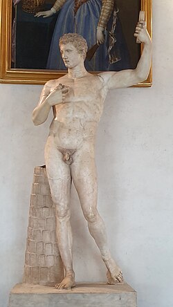 Mermerden çıplak genç erkek heykeli; sağ ayağa yüklenmiş contrapposto; sağ kol yukarıda, sol el göğüste; sağ bacak yanında silindirik destek; baş hafif sağa dönük.
Kaynak: https://en.wikipedia.org/wiki/Adonis